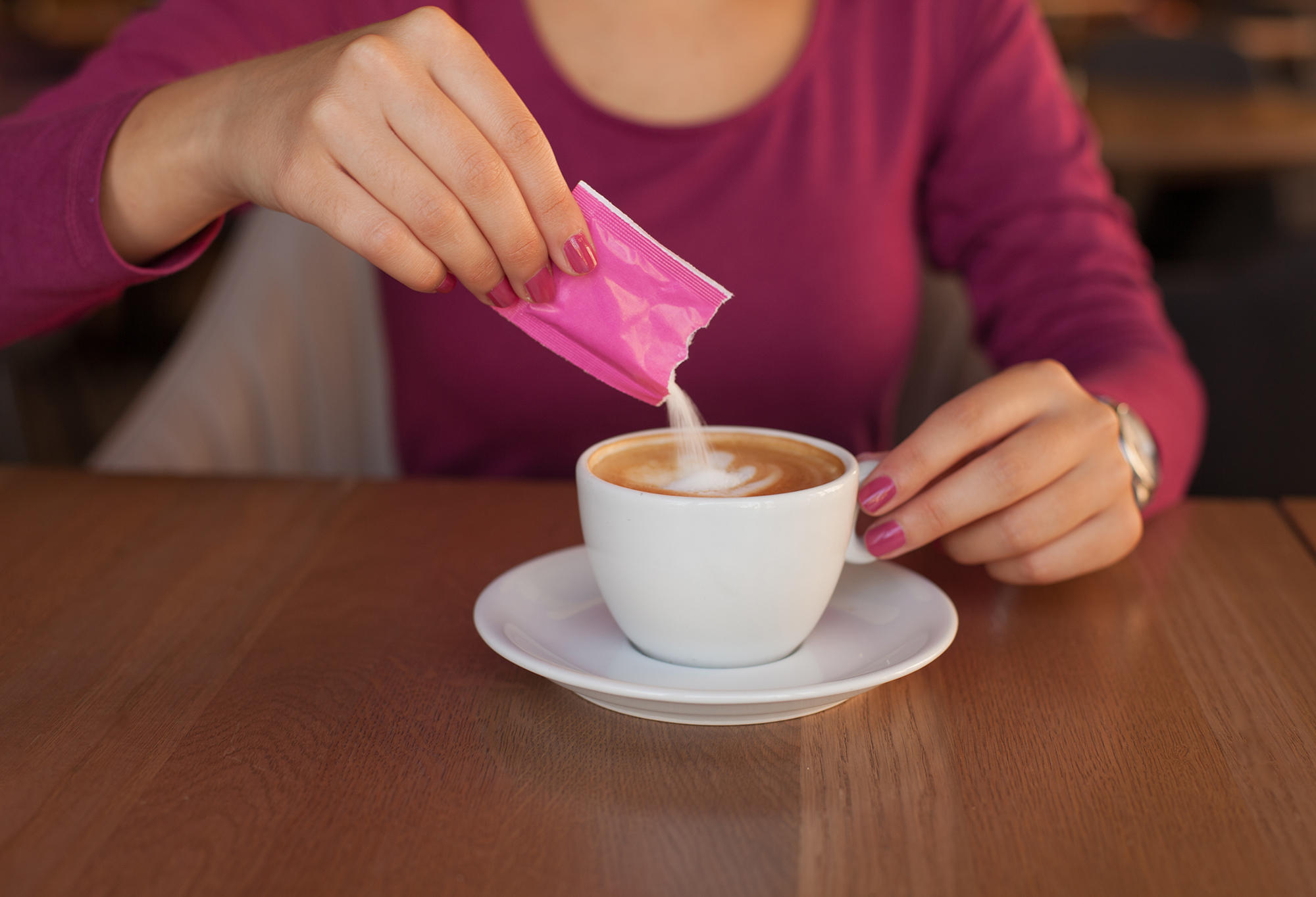 MÃO DE MULHER COLOCANDO ADOÇANTE NA XICARA DE CAFÉ